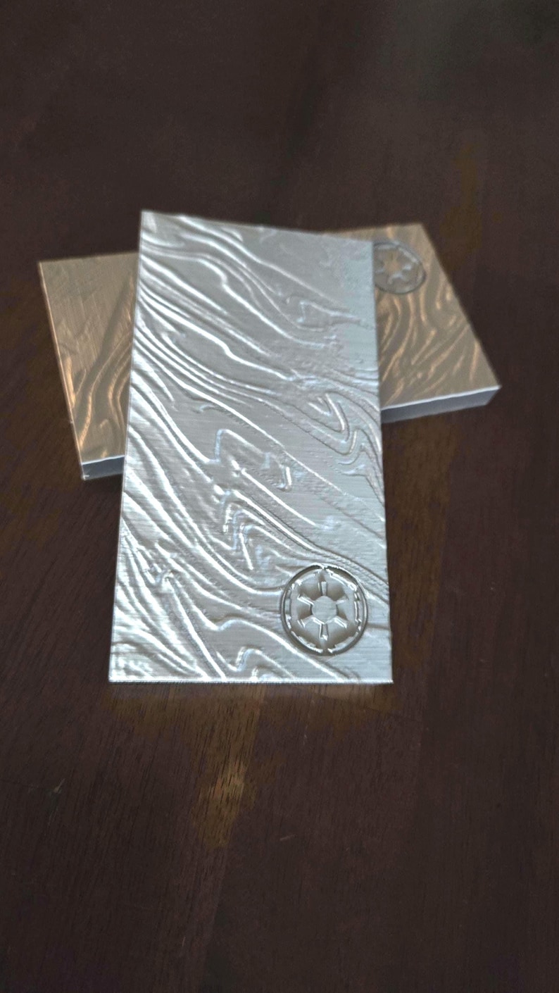 May include: Two silver metal business cards with a textured surface and a raised embossed logo of a star inside a circle.