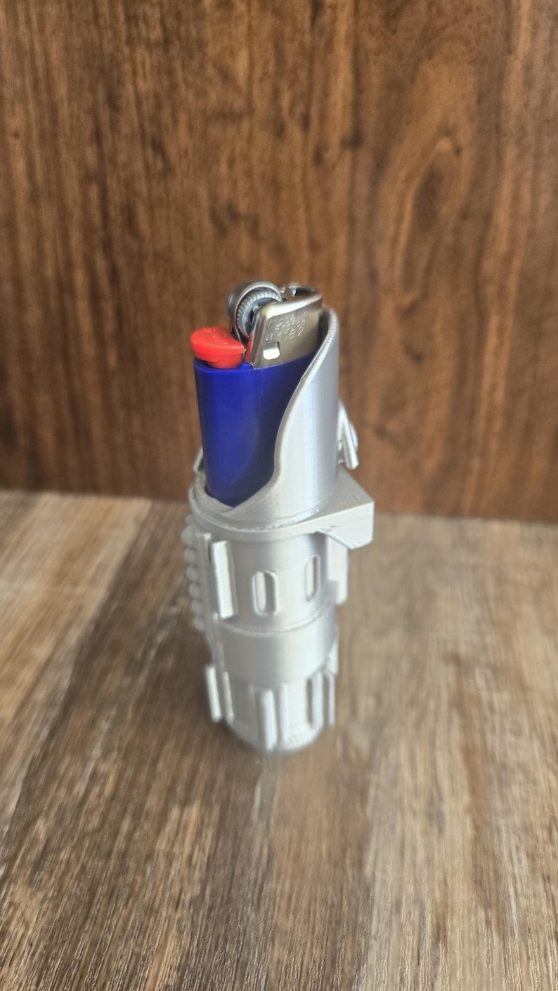 May include: A silver 3D printed lighter holder shaped like a lightsaber. A blue lighter is inserted into the holder.