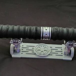 May include: A silver lightsaber with a black handle and red lightsabers on each end. The lightsaber is on a gray stand with a symbol on it.