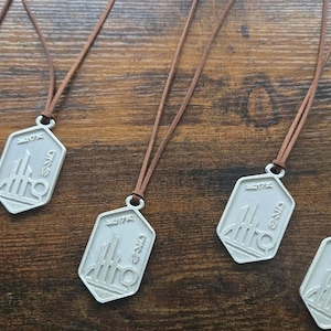 Peut inclure: Colliers avec pendentifs argentés et cordons en cuir marron. Chaque pendentif a un design unique et est de forme hexagonale. Les colliers sont disposés sur une surface en bois.