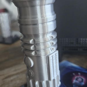 May include: A silver lightsaber lighter with a red button on top. The lighter is on a blue and black background.