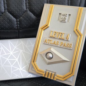 May include: A gold and silver key card with the text "Level 4 Atlas Pass".