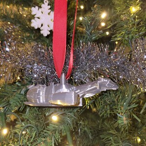 May include: A silver 3D printed ornament shaped like a spaceship hanging on a Christmas tree with a red ribbon and a white snowflake ornament.