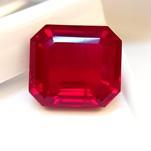 Puede incluir: Una gema roja oscura tallada en forma rectangular y facetada. La gema tiene una superficie pulida y brillante con múltiples facetas que reflejan la luz. El color es un rojo rico y saturado.