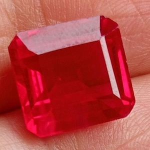 Könnte beinhalten: Ein tiefroter Edelstein mit quadratischem Smaragdschliff. Der Edelstein ist facettiert und hochglanzpoliert.