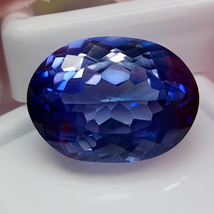 Può includere: Una gemma sfaccettata di forma ovale con una tonalità blu intenso. La superficie della gemma riflette la luce, creando un effetto scintillante. La pietra è posta su uno sfondo bianco, che ne evidenzia il colore e il taglio. Questa gemma è adatta per gioielli.