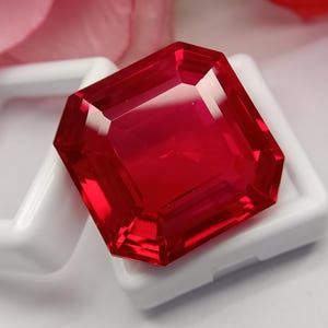 Puede incluir: Una gema de color rojo intenso y vibrante con un corte octogonal facetado. La piedra presenta bordes afilados y limpios y una superficie pulida altamente reflectante que atrapa la luz, creando brillos intensos sobre su cuerpo carmesí transparente.