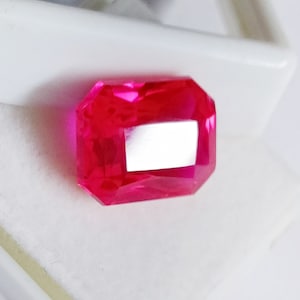 Op de afbeelding: Een levendige roze edelsteen met een rechthoekige vorm en een facetgeslepen snit. De edelsteen is gezet in een heldere, beschermende zetting.