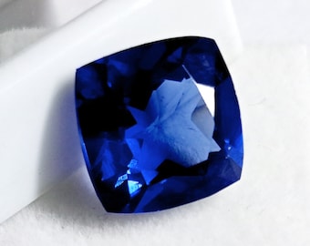 Può includere: Una pietra preziosa blu scuro con taglio a cuscino quadrato. La pietra preziosa è sfaccettata e ha un'alta lucidatura.