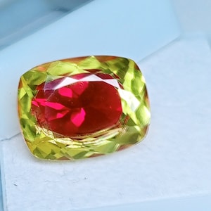May include: A red gemstone with a yellow and green outer layer, cut into a rectangular shape.