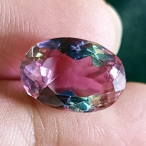 Op de afbeelding: Een grote, ovale edelsteen met een iriserende kleur in roze, paars en groen.
