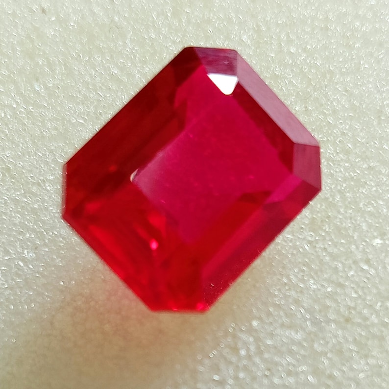 May include: A deep red emerald cut gemstone with a high polish.