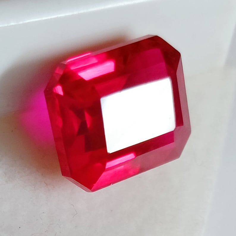 May include: A deep red, emerald-cut gemstone with a high polish.