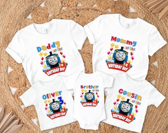 May include: White t-shirts with colorful graphics featuring Thomas the Tank Engine. Designs include "Daddy of the Birthday Boy," "Mommy of the Birthday Boy," "Oliver 3," "Brother of the Birthday Boy," and "Cousin of the Birthday Boy."