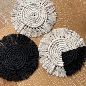 May include: Three round crocheted coasters with fringe. One coaster is black, one is white, and one is half white and half black.
