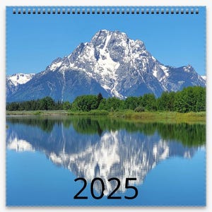 May include: A calendar with a photo of a snow-capped mountain reflected in a still lake. The year 2025 is printed in black at the bottom of the image.