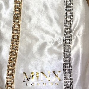 May include: Two rhinestone bracelets, one gold-toned and one silver-toned, are displayed on a white satin surface. The bracelets are rectangular with square-shaped rhinestones. The gold bracelet is on the left, and the silver bracelet is on the right.