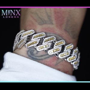 May include: A silver-toned bracelet with yellow and clear gemstones. The bracelet is a cuban link style with a white shirt in the background. The brand name "MINX LONDON" is visible in the top left corner.