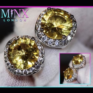 Könnte beinhalten: Ein Paar silberne Ohrringe mit großen gelben Edelsteinen, die von einem Heiligenschein aus kleineren klaren Edelsteinen umgeben sind.