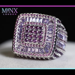 May include: A square-shaped ring with a silver band and a dazzling array of purple and pink gemstones. The ring features a central square of small, dark purple stones, surrounded by layers of larger, rectangular and square-cut gems. The brand name "MINX LONDON" is visible.