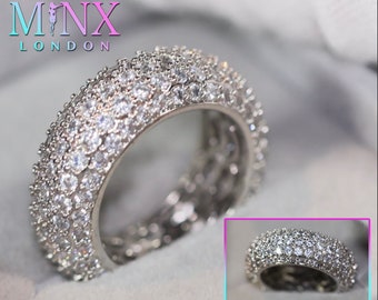Könnte beinhalten: Ein silberner Ring mit mehreren Reihen aus klaren Zirkonia-Steinen. Der Ring liegt auf einer grauen Oberfläche.  MINX LONDON ist in der oberen linken Ecke des Bildes gedruckt.