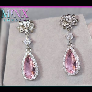 Könnte beinhalten: Ein Paar silberne Ohrhänger mit einem rosafarbenen birnenförmigen Edelstein, der von kleineren klaren Edelsteinen umgeben ist. Die Ohrringe haben oben ein zartes Blumenmuster.