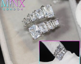 May include: A silver-toned ring with multiple square-cut, clear gemstones. The ring features a wrap-around design with the gemstones arranged in a linear fashion. The brand name "MINX LONDON" is visible in the upper left corner.