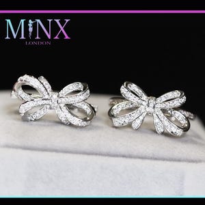 Puede incluir: Un par de pendientes de plata en forma de lazo con piedras de circonita cúbica transparentes.