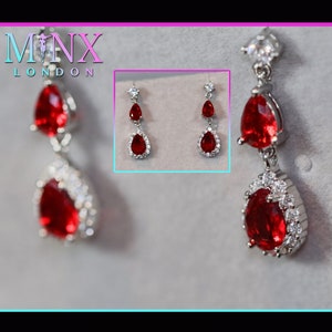 May include: A pair of silver dangle earrings with red pear-shaped gemstones and clear crystal accents.