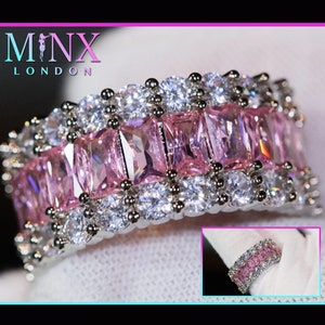 May include: A silver ring featuring a row of pink rectangular stones surrounded by smaller clear stones.