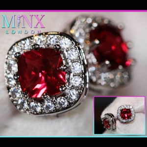 May include: A pair of silver earrings with a large red square-shaped gemstone surrounded by smaller white gemstones.