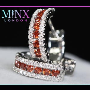 May include: Silver hoop earrings with a double row of orange and white gemstones.