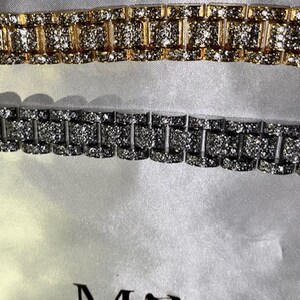 May include: Two rhinestone-studded bracelets. One is gold-toned, the other silver-toned. The bracelets have a watch band style with rectangular links. The background is a soft, white fabric.