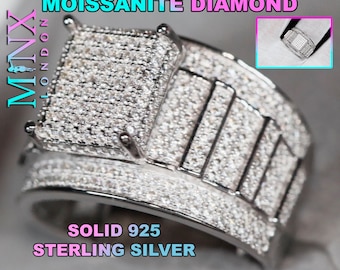 Puede incluir: Un anillo de plata con una gran piedra central de forma cuadrada rodeada de piedras más pequeñas. La banda también está cubierta de piedras pequeñas. El anillo está etiquetado como "MOISSANITE DIAMOND" y "SOLID 925 STERLING SILVER".
