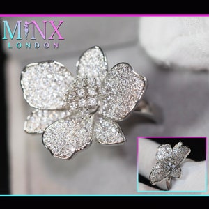 May include: A silver ring featuring a large, sparkling flower design. The flower is crafted from numerous small, clear stones.