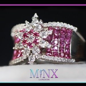 May include: A silver ring with a striking design, featuring pink and white gemstones. The ring showcases a central section of square-cut pink stones, complemented by smaller white stones. The ring has the text "MINX LONDON".