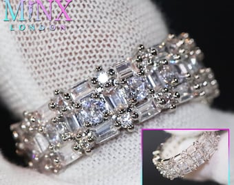 May include: A silver ring with a row of square and rectangular clear stones set in a pave setting. The ring is on a white surface.