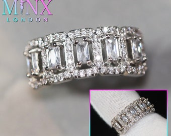 May include: A silver ring with a row of rectangular clear stones set in a pave setting. The stones are surrounded by smaller clear stones.