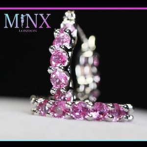 Puede incluir: Un par de pendientes de aro de plata con piedras preciosas rosas. Los pendientes son pequeños y delicados.