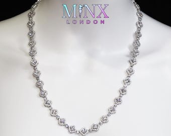May include: A silver-toned necklace with a repeating floral design, set with clear gemstones. The necklace is displayed on a white mannequin. The brand name "MINX LONDON" is visible in the upper center.