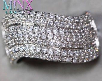 May include: A silver ring with multiple rows of small, clear cubic zirconia stones. The ring is curved and has a polished finish.