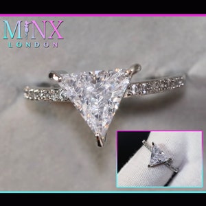 Puede incluir: Un anillo de plata con una gran piedra triangular transparente engastada en el centro. La banda está decorada con piedras transparentes más pequeñas.