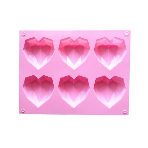 May include: Pink silicone mold with six heart-shaped cavities. Each heart has a geometric design.
