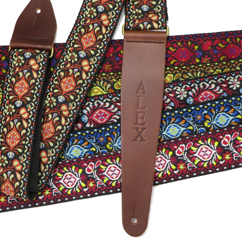 May include: A colorful guitar strap with a brown leather end piece that has the name "ALEX" embossed on it.