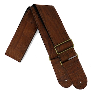 May include: A brown guitar strap made of cork with adjustable straps and brass buckles.