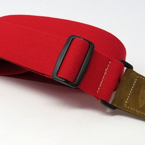 May include: Red guitar strap with a black buckle and a brown suede end piece with a guitar keyhole.