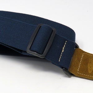 May include: A dark blue guitar strap with a brown leather end and a black metal buckle.