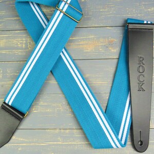 May include: A turquoise and white guitar strap with black leather ends. The strap has the word "ROCK" embossed on one end.