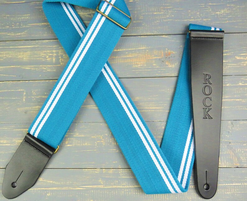 May include: A turquoise and white guitar strap with black leather ends. The strap has the word "ROCK" embossed on one end.