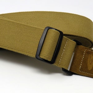 May include: A tan guitar strap with a black adjustable buckle and a brown suede end piece with a logo.